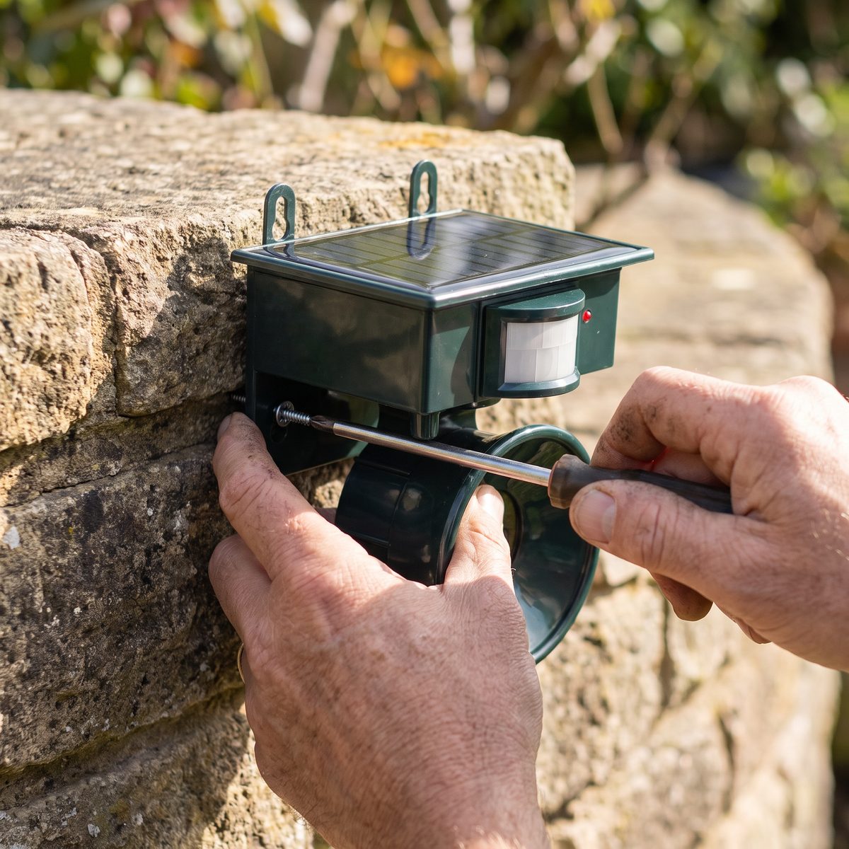 Two hands driving a screw through the bracket into a garden wall