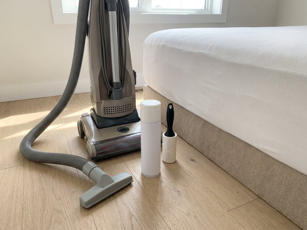 An upright vacuum, a spray can and a lint roller by a bed